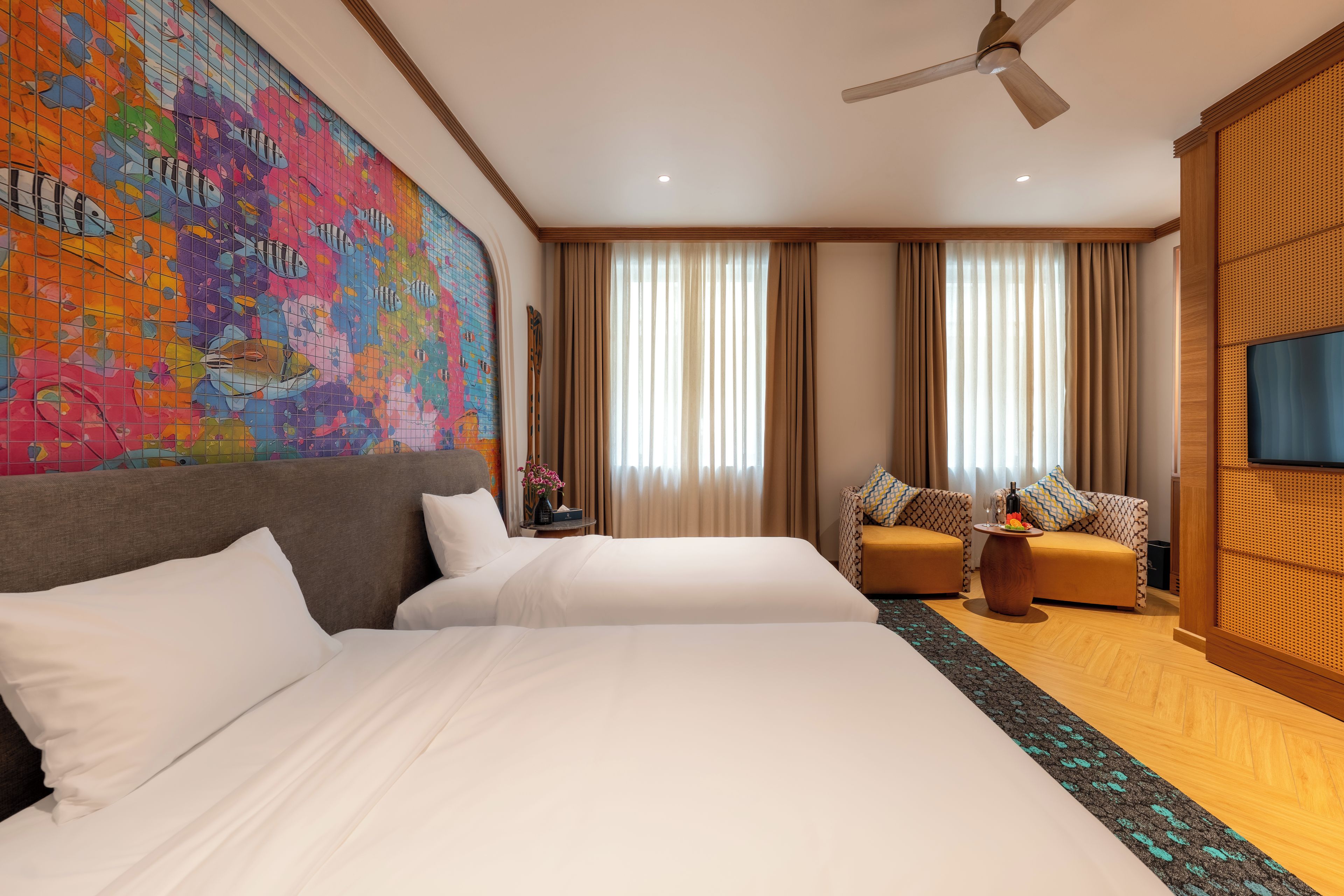Una habitación de hotel con una cama grande, dos sofás, un televisor y un ventilador de techo.
