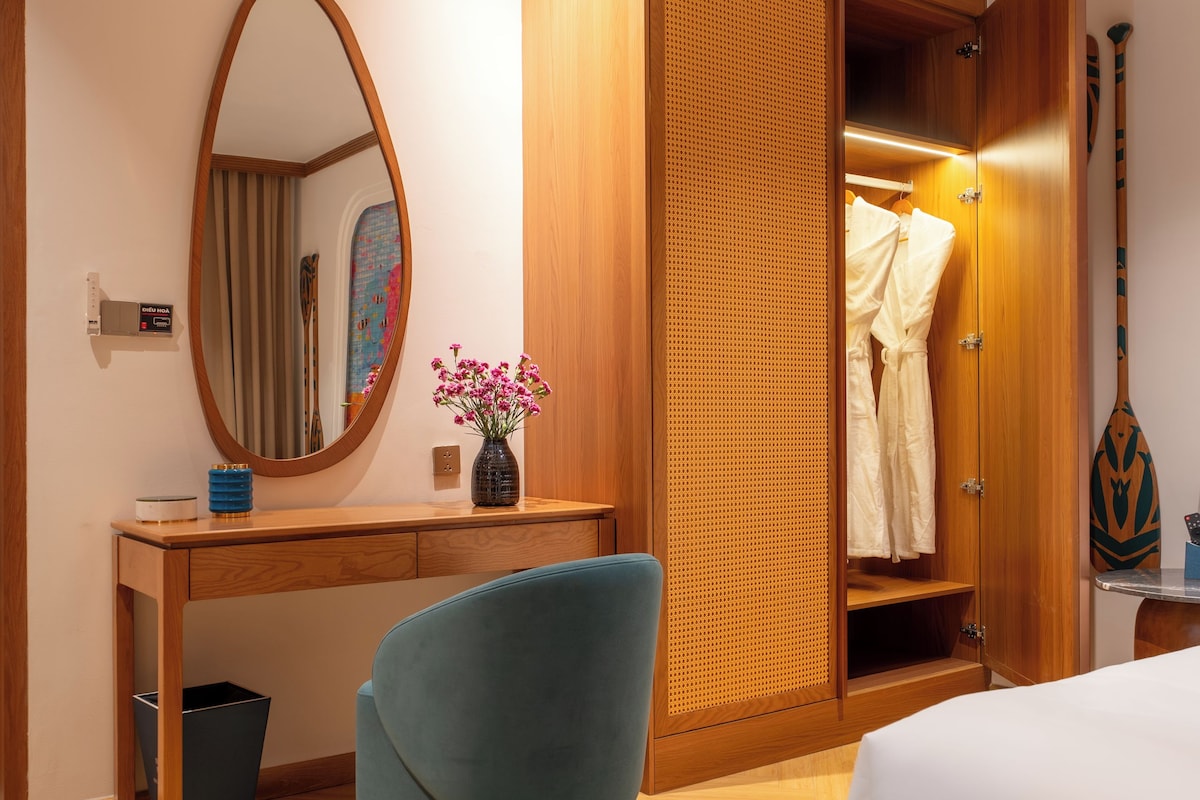 A hotel room with a bed, a desk, a chair, a wardrobe, and a mirror.