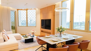 Un salon moderne avec un canapé, une table à manger pour quatre personnes et un téléviseur fixé au mur.