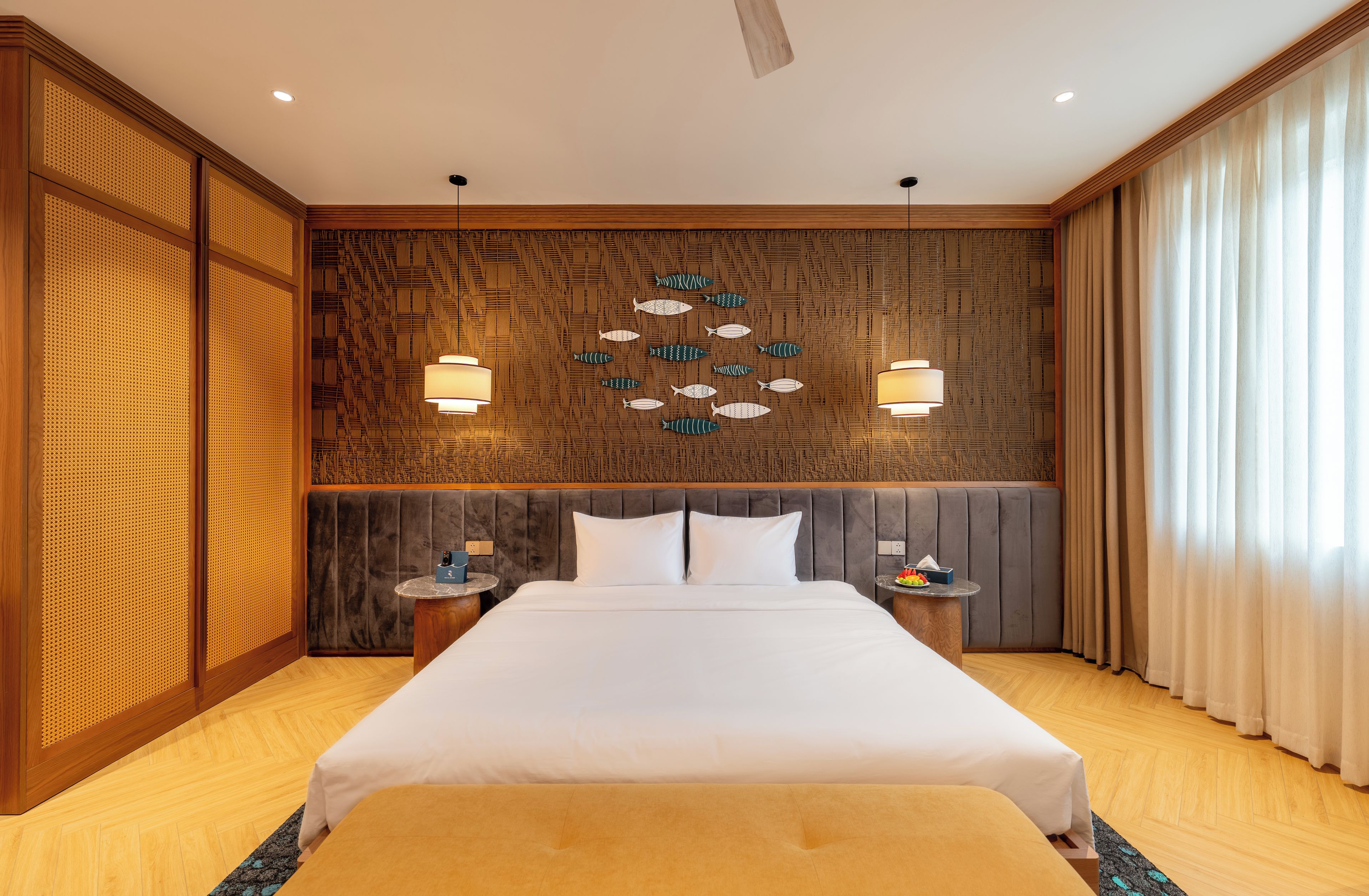 Habitación de hotel con una cama grande, dos mesitas de noche, una pared con diseño geométrico y un ventilador de techo.