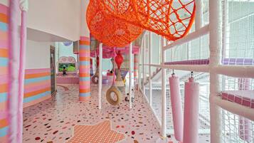 A brightly lit indoor play area with colorful walls, a star-patterned floor, and netted play structures.