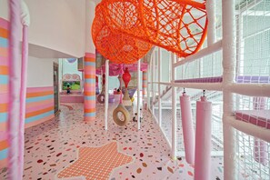 A brightly lit indoor play area with colorful walls, a star-patterned floor, and netted play structures.