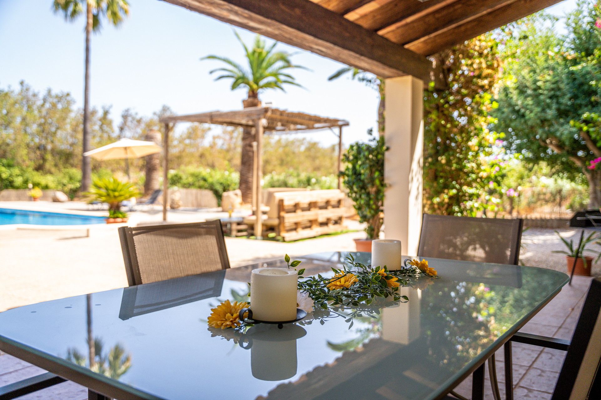 Eine Terrassengruppe im Freien mit Glastisch, Stühlen, einer Kerze und Blumenarrangements.