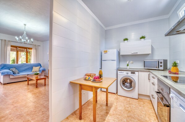Un espace de vie compact comprenant un canapé, une petite table, un lave-linge, un four à micro-ondes et un réfrigérateur.