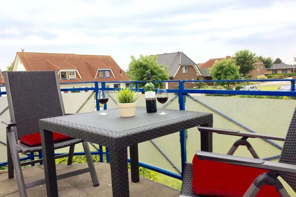 An outdoor seating area with wicker chairs and a table, a bottle of wine, and a glass on the table.