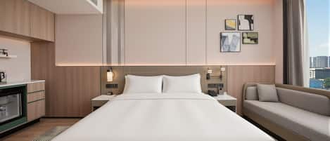 A hotel room with a large bed, a sofa, a desk with a lamp, and artwork on the wall.