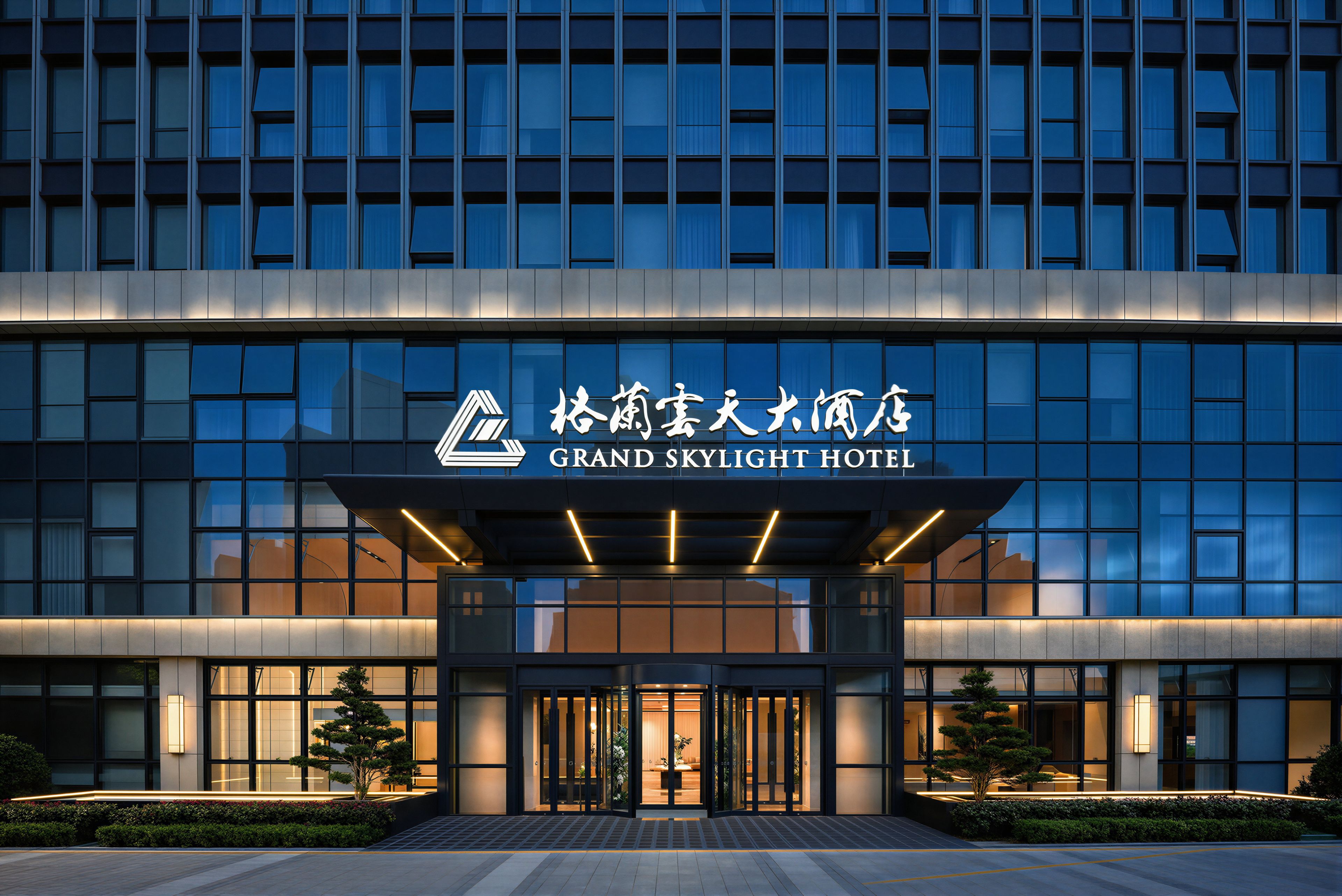 A modern hotel entrance with a large sign, glass facade, and well-lit entrance.