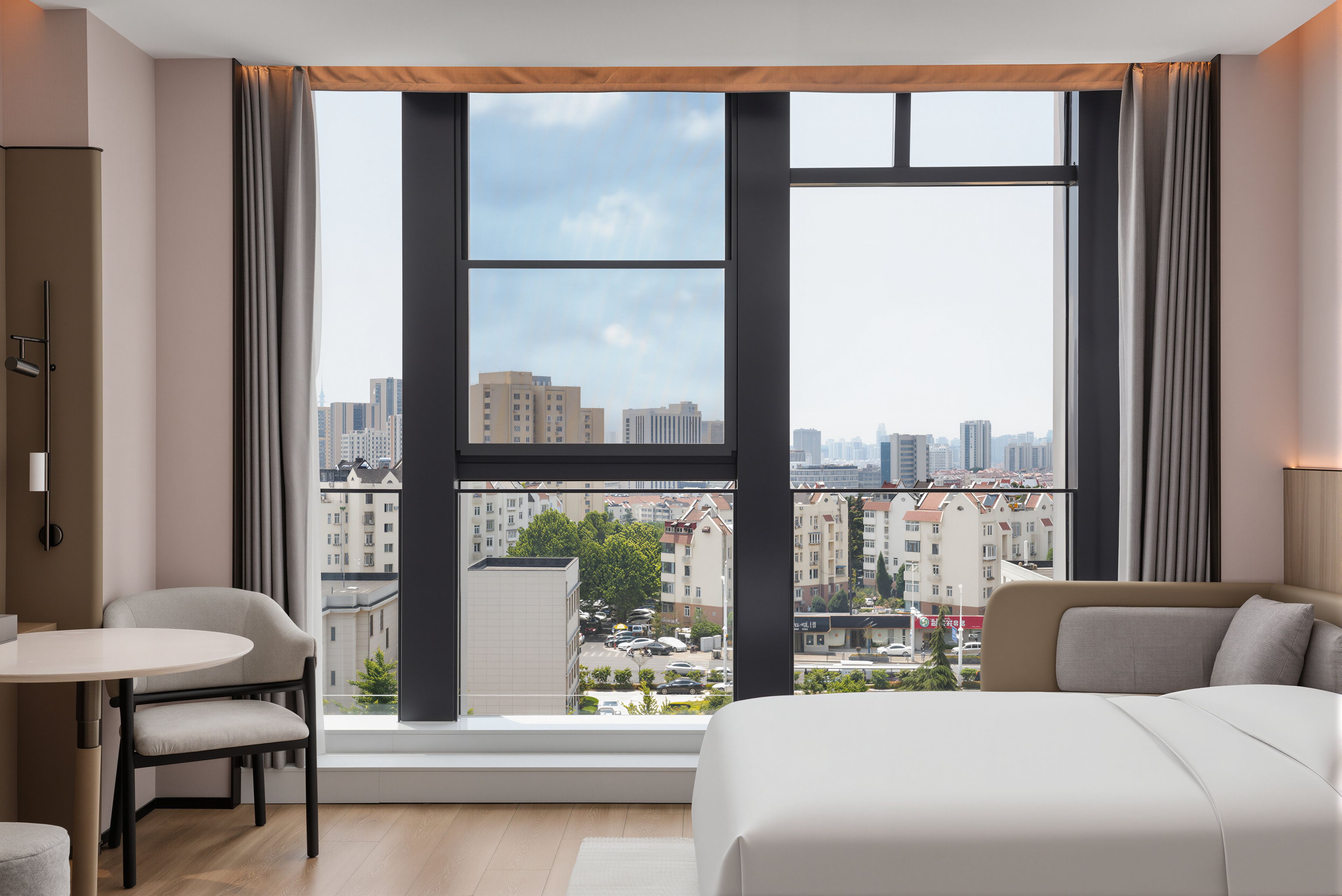 Quarto de hotel moderno com uma janela grande, cama, escrivaninha e cadeira.
