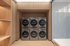 A laundry room with six stacked appliances, including a dryer and a washer, in a modern setting with wooden cabinetry and a tiled floor.
