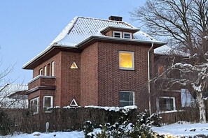 A two-story brick house with a snow-covered roof and a visible yellow-lit window. - Wendland-am-Weinberg (Hitzacker)