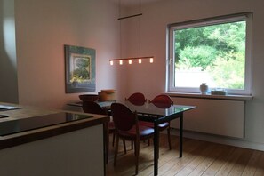 A dining area with a glass table, red chairs, a pendant light, and a window with a view of greenery. - Wendland-am-Weinberg (Hitzacker)