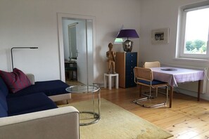 Et værelse med sofa, bord med stol, lampe, statue og et vindue.