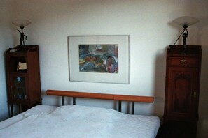 A bedroom with a bed, a framed abstract painting, and two wooden cabinets with lamps. - Wendland-am-Weinberg (Hitzacker)