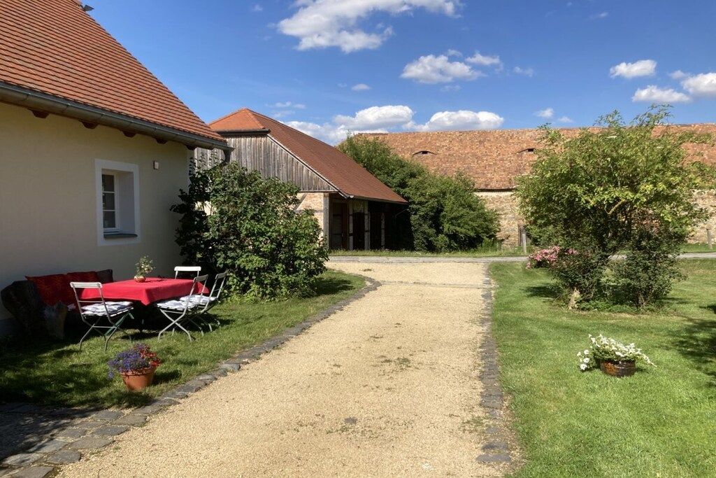 A house with a gravel driveway, a red table with chairs, and a brick wall in the background.
