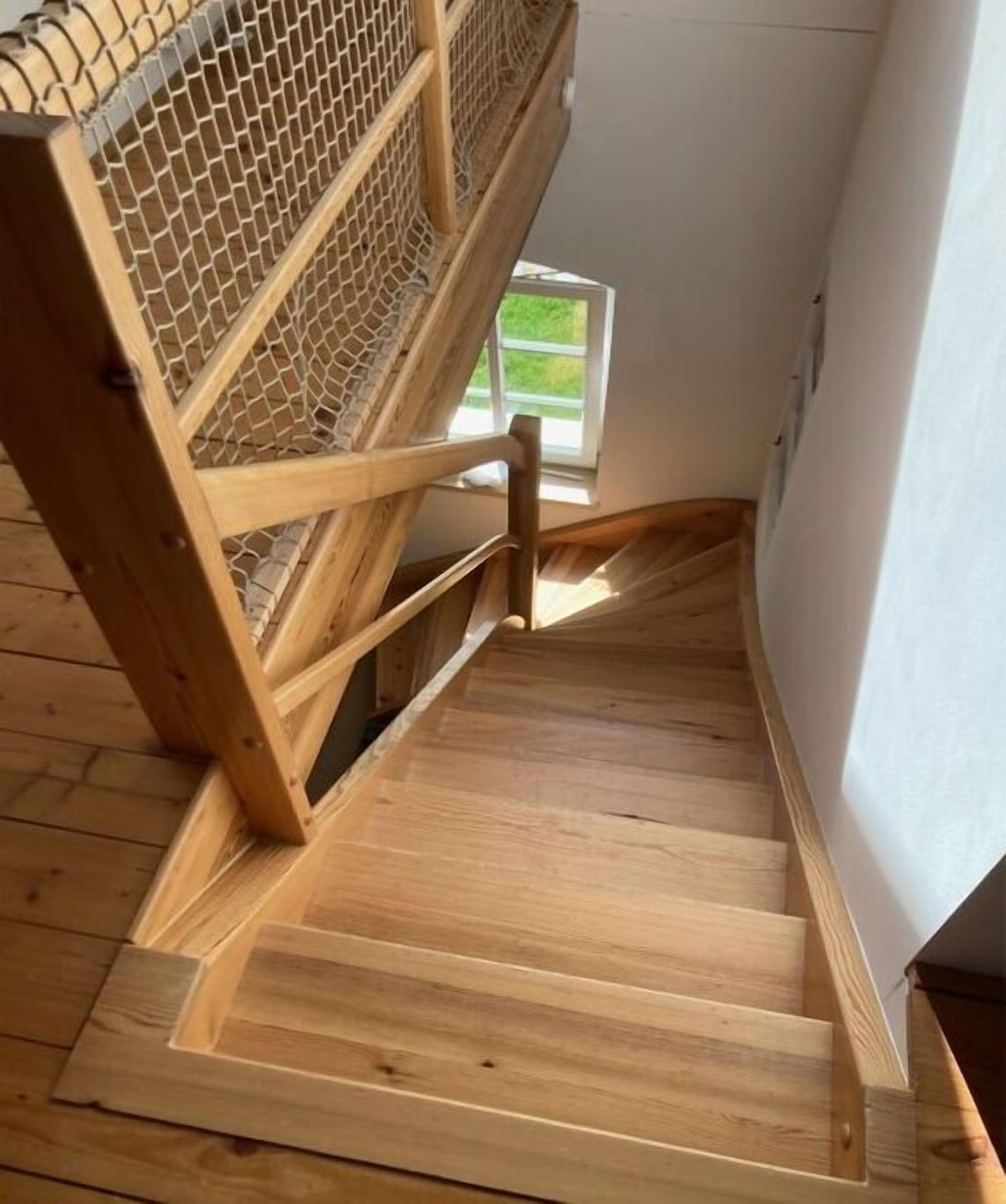 A wooden staircase with a mesh railing, leading to an upper level.
