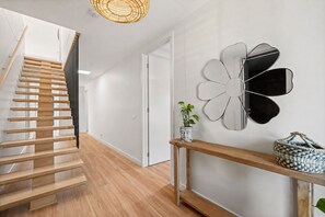 A modern interior with a wooden staircase, a wall-mounted mirror, and a woven bag on a console table. - The Perch San Remo - an Incredible View by Ready Set Stay (San Remo)