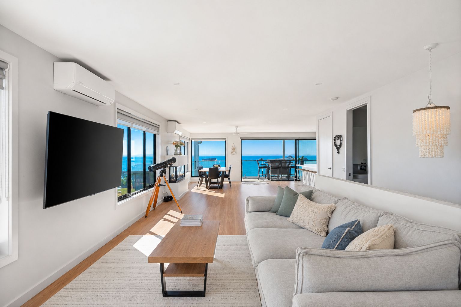 A modern living room with a flat-screen TV, a telescope, a wooden coffee table, and a sofa with cushions.