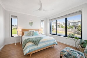 A bedroom with a bed, a nightstand, a ceiling fan, and large windows. - The Perch San Remo - an Incredible View by Ready Set Stay (San Remo)