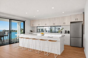 A modern kitchen with a large island, bar stools, and a view of the outdoors. - The Perch San Remo - an Incredible View by Ready Set Stay (San Remo)