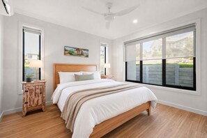 A bedroom with a wooden bed, two bedside tables, a ceiling fan, and large windows. - The Perch San Remo - an Incredible View by Ready Set Stay (San Remo)