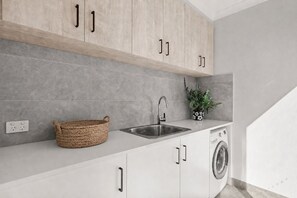 A modern kitchen with a built-in washing machine, a sink, and a basket. - The Perch San Remo - an Incredible View by Ready Set Stay (San Remo)