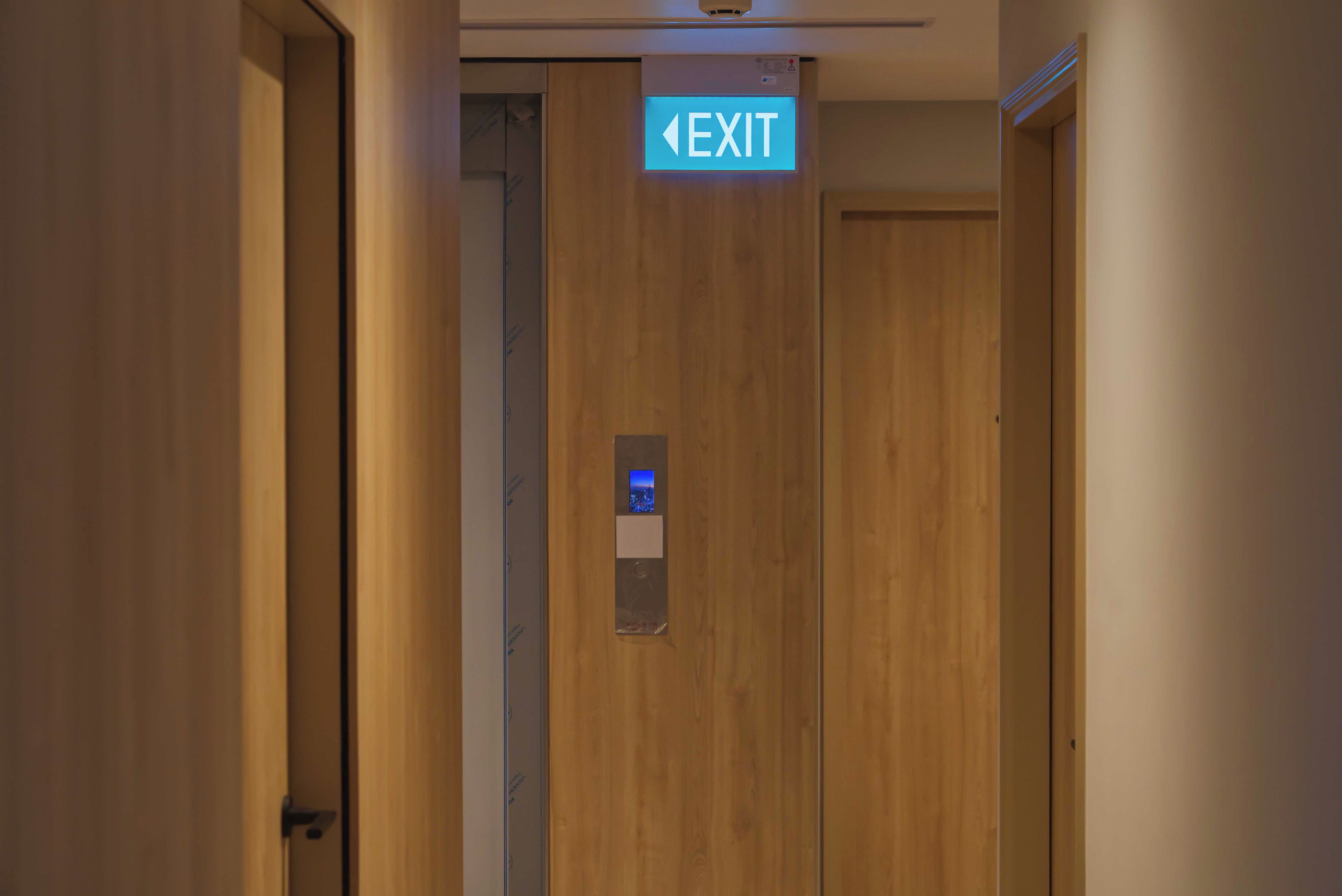 Een gang met een houten deur en een pictogram met de tekst EXIT erboven.