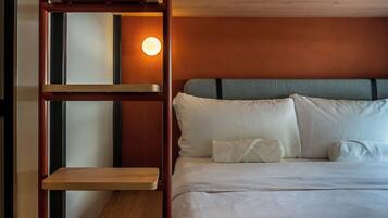 Una habitación de hotel con una cama, una escalera de madera y una lámpara fijada a la pared.