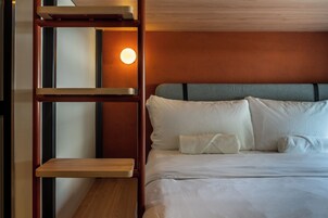 Una habitación de hotel con una cama, una escalera de madera y una lámpara fijada a la pared.