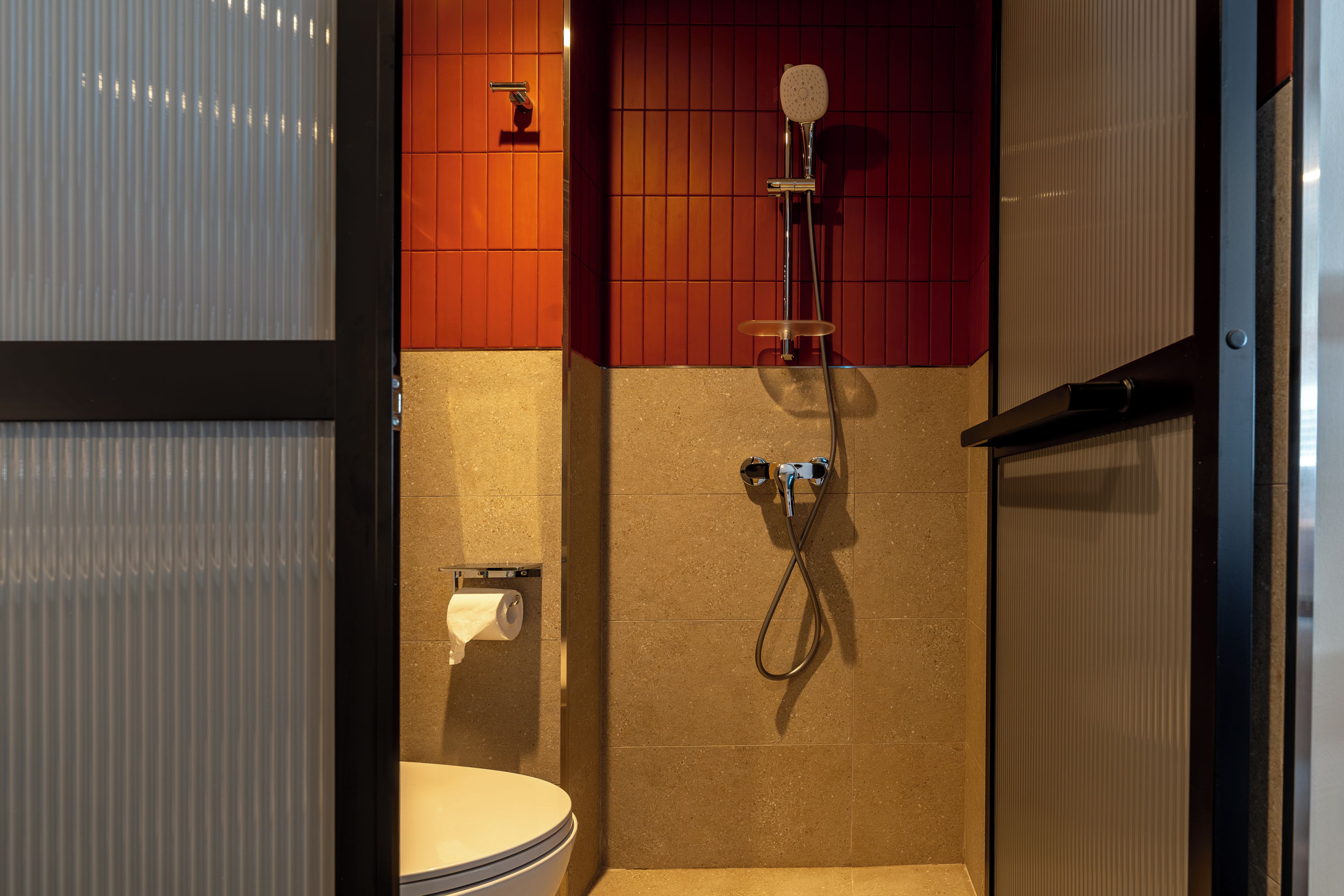 A compact bathroom with a shower, toilet, and a paper towel dispenser.