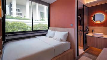 Habitación de hotel con cama, baño con lavamanos y espejo, y vista a zonas verdes.
