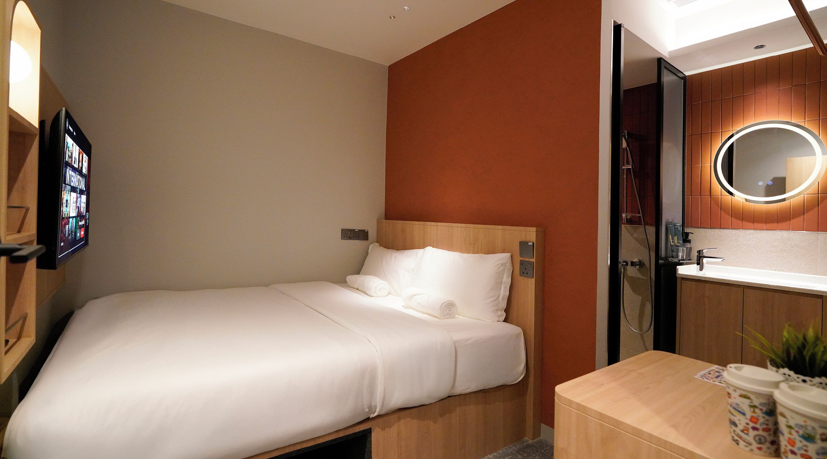 Een hotelkamer met een bed, nachtkastje, spiegel en een aan de muur bevestigde televisie.