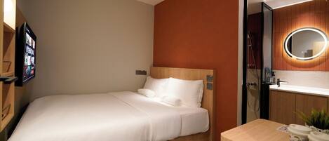 Une chambre d’hôtel équipée d’un lit, d’une table de chevet, d’un miroir et d’un téléviseur fixé au mur.
