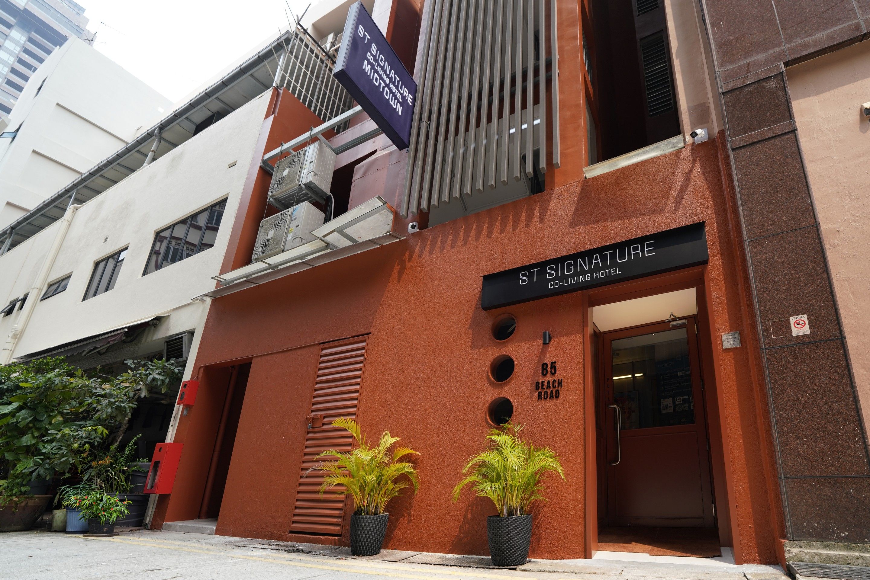 A hotel entrance with a sign reading 'St Signature Co-Living Hotel' and a number '85' indicating the address.