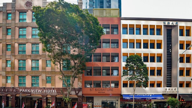 Un hotel de varios pisos con un llamativo letrero que dice 'PARK VIEW HOTEL', un edificio 'ST SIGNATURE' y un edificio 'CHIVE SING BUILDING' con una escalera visible.