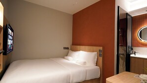 A hotel room with a bed, a small table, a mirror, and a TV displaying a program. - ST Signature Midtown (Singapore)