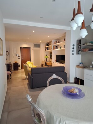 Sala de estar moderna com sofá, mesa de jantar e área de cozinha ao fundo.