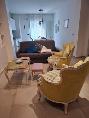 Sala de estar com sofá, poltronas, mesa de centro e um espaço de jantar ao fundo.