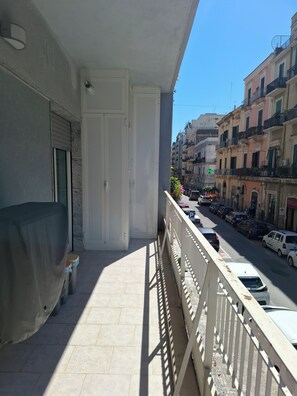 A balcony with a covered seating area, a door, and a view of a street with parked cars and buildings. - The Perfect Home for Remote Work and Vacations: Living in Downtown Bari (Bari)