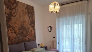 A bedroom with a large bed, a chair, a painting on the wall, and a window with curtains. - Vrbo Property (Bari)