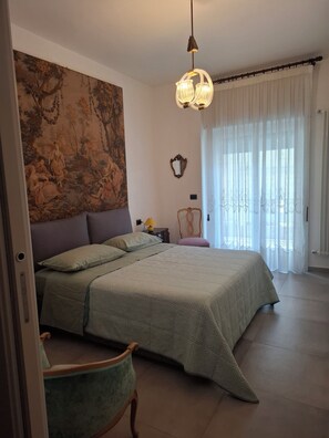 Quarto com cama grande, uma cadeira, um quadro na parede e janela com cortinas.