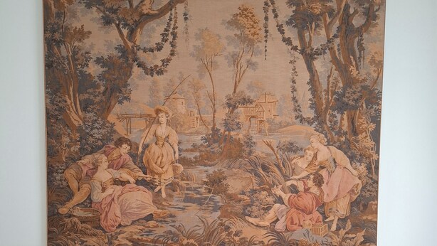 A bed with a large tapestry depicting a pastoral scene, two pillows, and a nightstand with a lamp. - Vrbo Property (Bari)