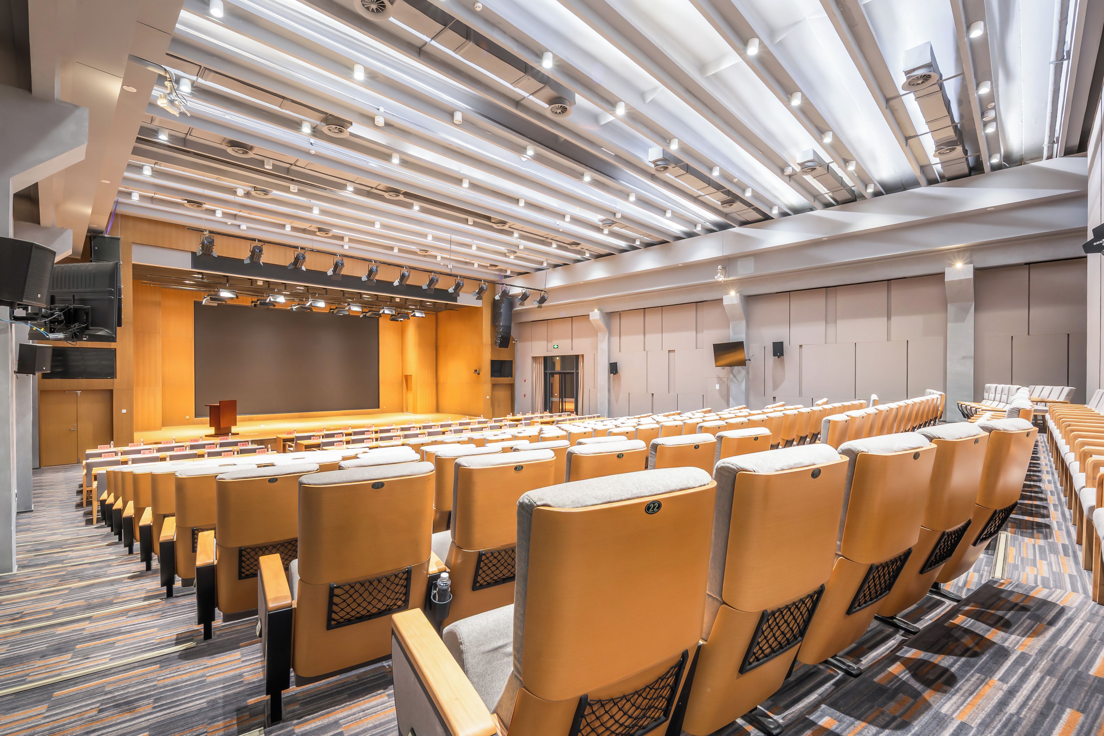 A conference room with rows of chairs, a stage, and a large screen.