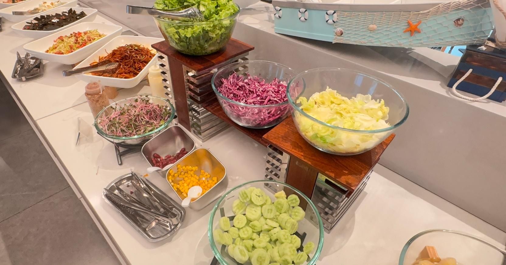 A buffet table with various food items including salads, shredded vegetables, and sliced cucumbers.
