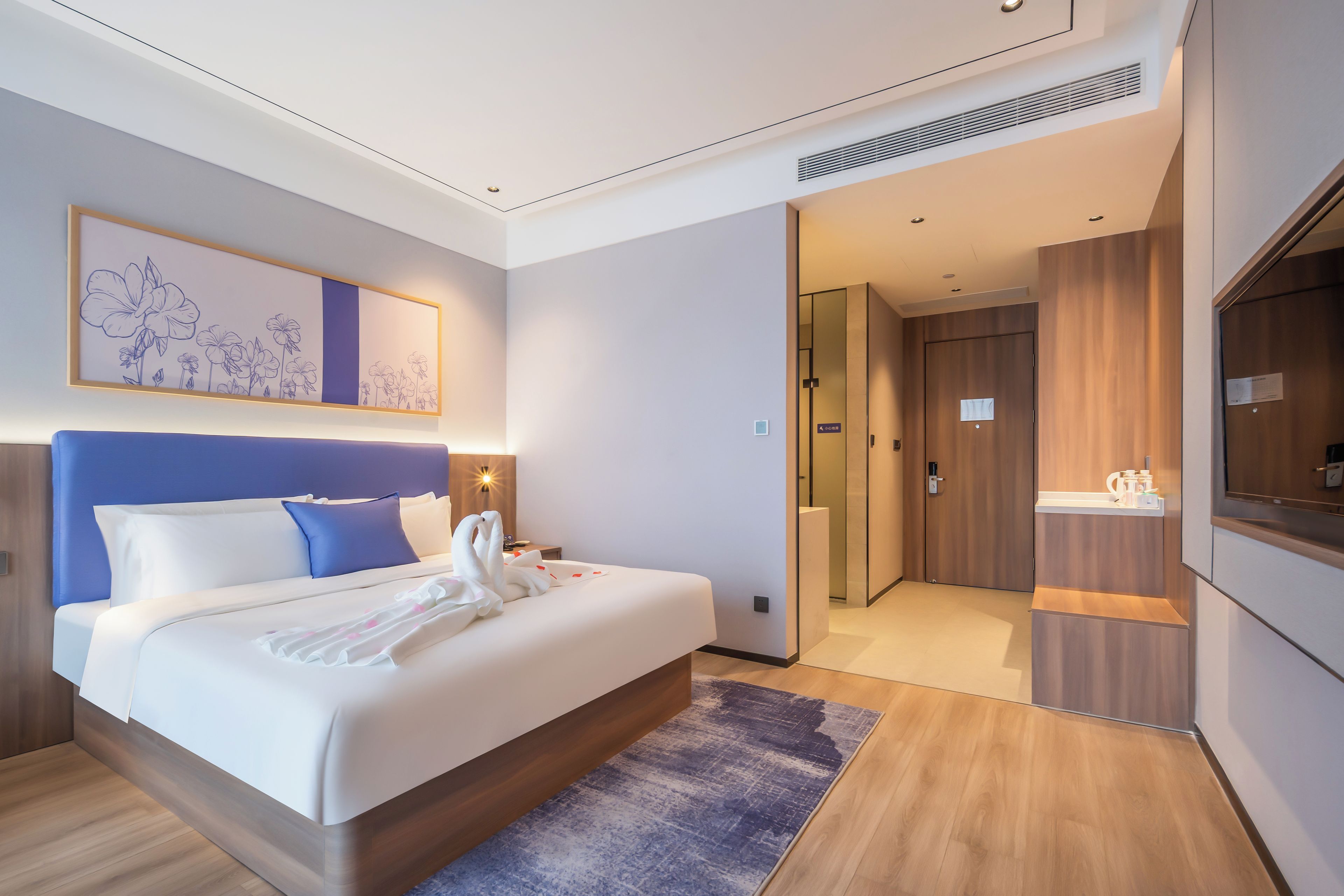 A modern hotel room with a large bed, a bathroom with a shower, and a small sitting area.