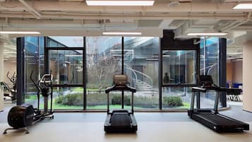 A gym with exercise equipment, large windows, and a view of the outside.