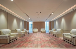 A hotel room with a large, patterned carpet, multiple seating areas, and a view through a large window.