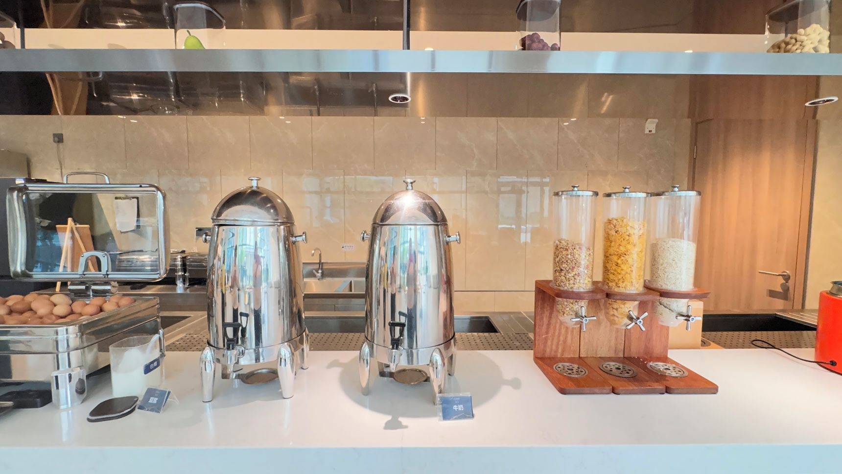 A buffet area with stainless steel dispensers for beverages and a wooden rack with jars of condiments.