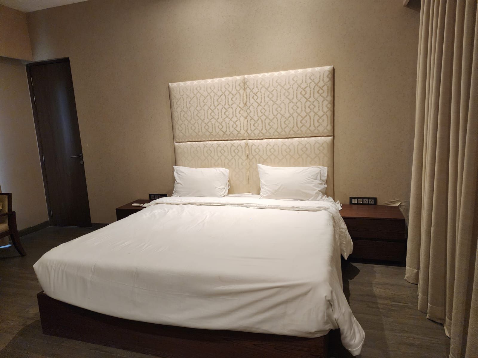 Una habitación de hotel con una cama grande, un cabecero de diseño geométrico, dos mesitas de noche y una puerta.