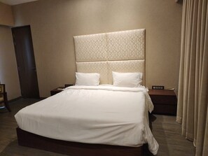 A hotel room with a large bed, a headboard with a geometric pattern, two bedside tables, and a door.