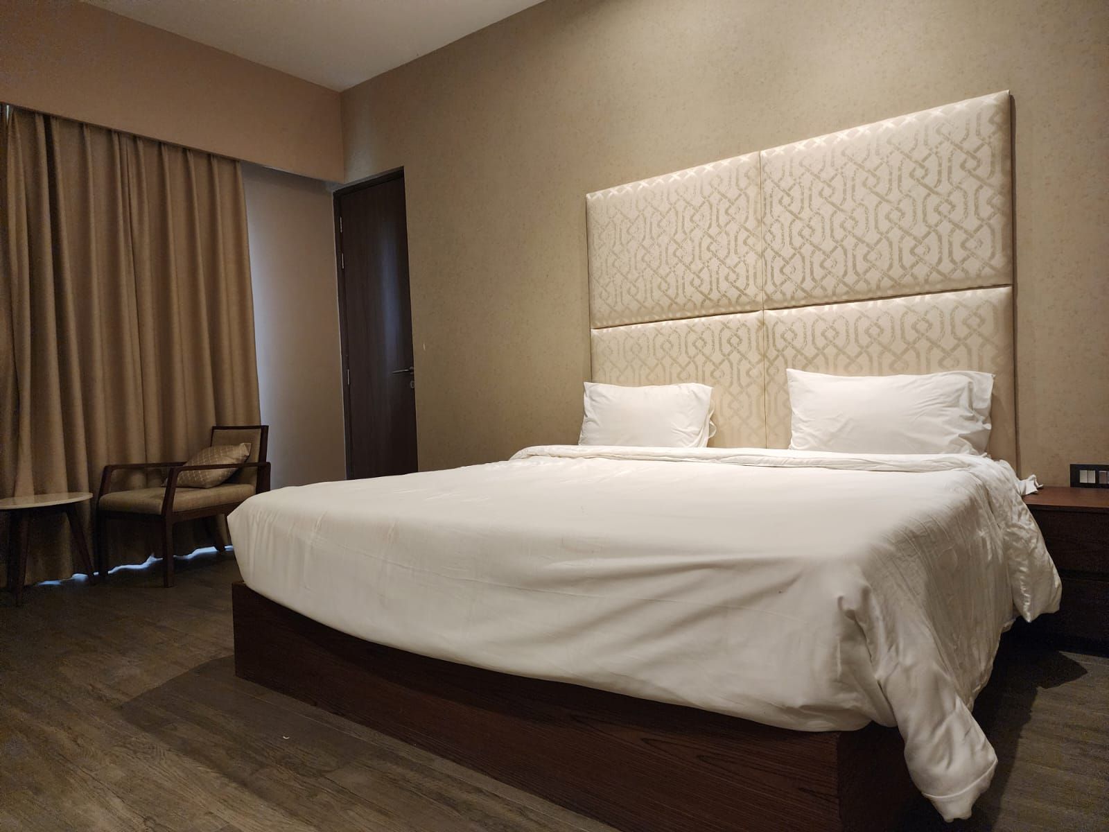 A hotel room with a large bed, a chair, a wardrobe, and a door.